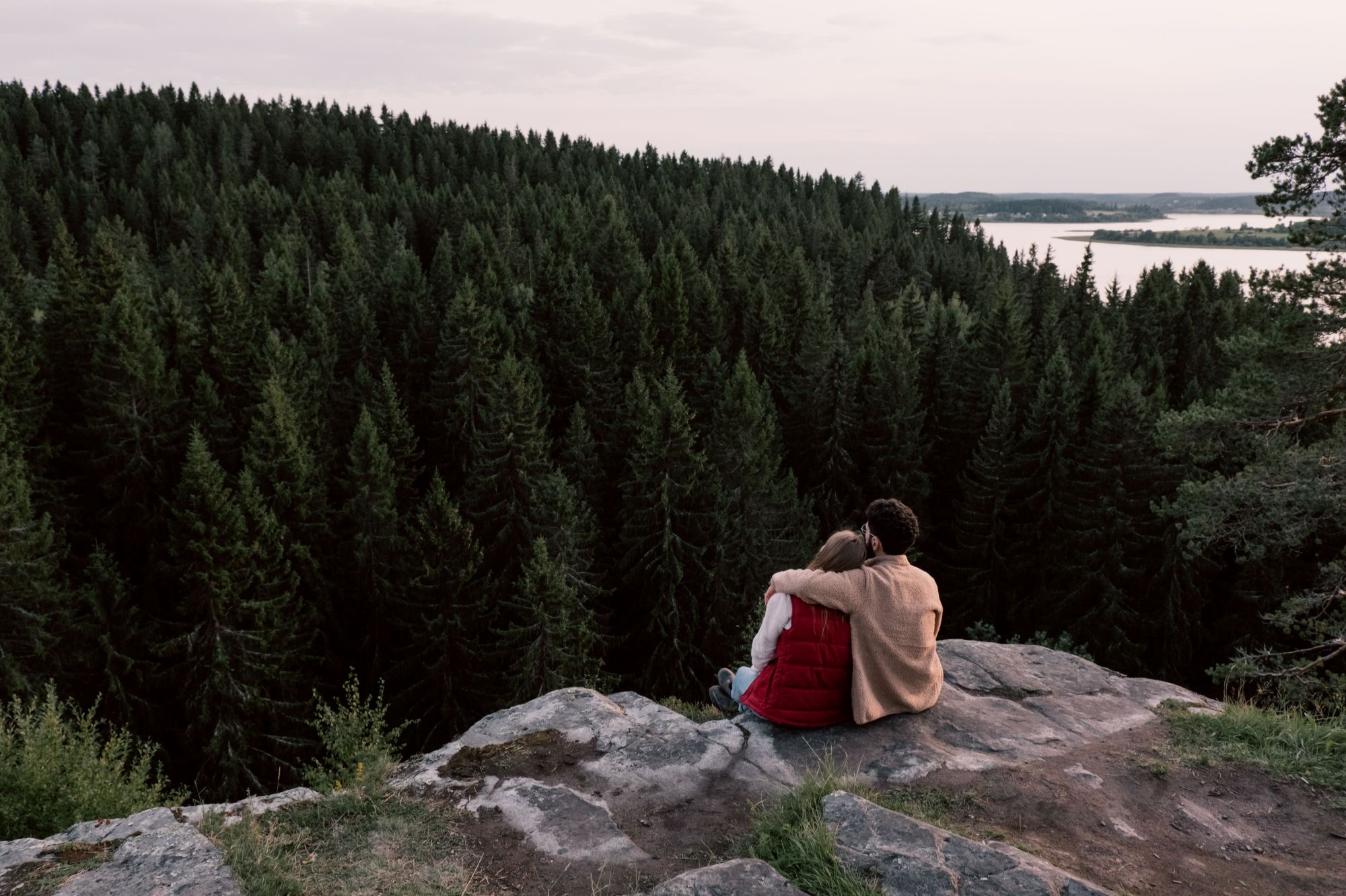 Ein Paar sitzt eng beieinander auf einem Felsen über dem Wald