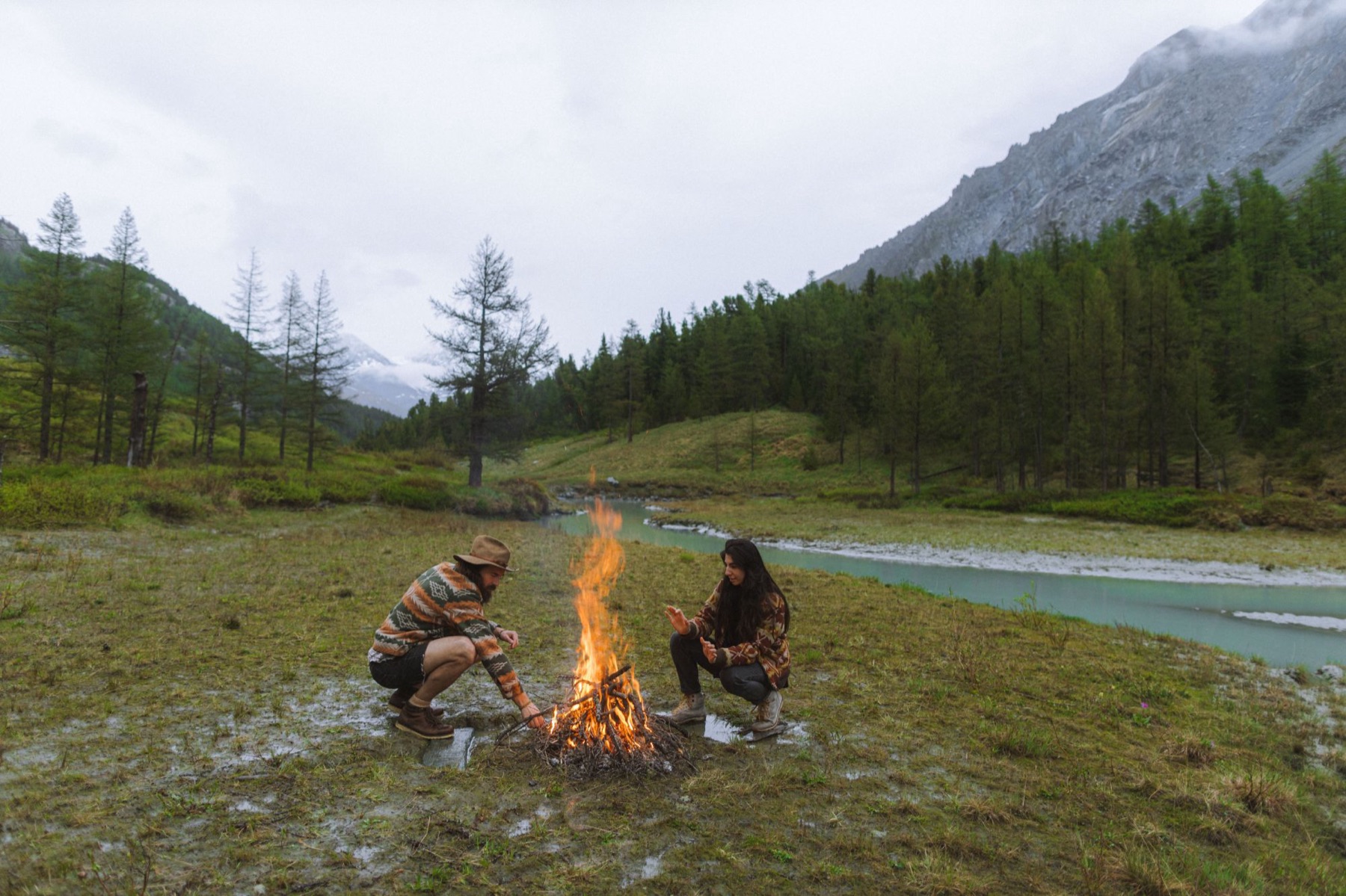 Ein Paar am Feuer an einem Fluss in den Bergen