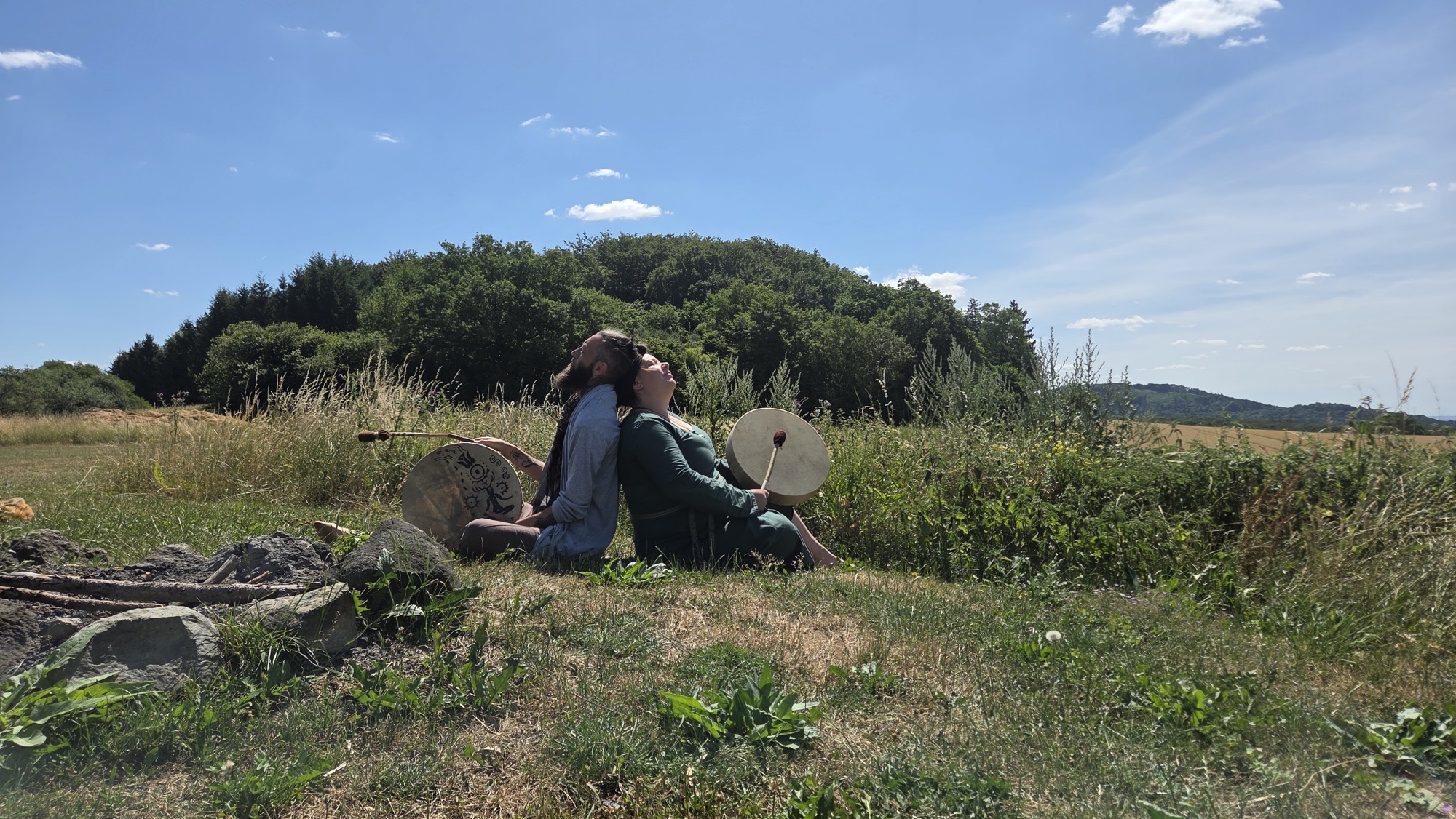 Nico and Sarah sitting back to back with their drums in a meadow